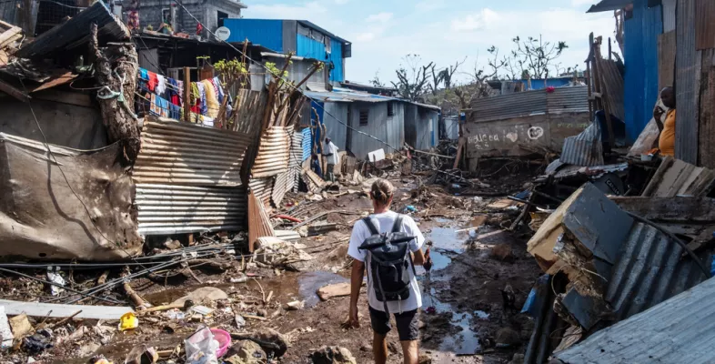 Mitarbeitender geht durch zerstörtes Viertel aus Blechhütten
