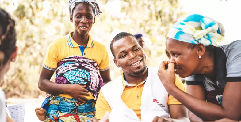 Mitarbeiter in Benin, sitzend im Gespräch mit zwei Frauen