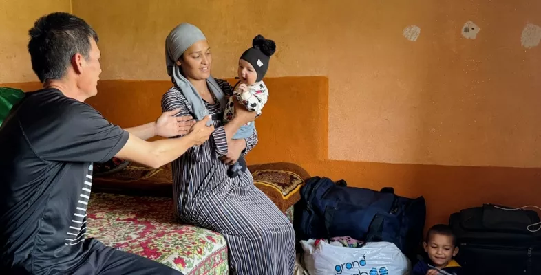 Vater öffnet Arme Richtung Mutter, die Baby hält