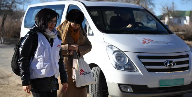 Zwei Mitarbeitende laufen vor Fahrzeug über Straße