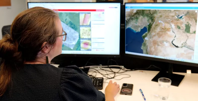Ann De Schutter sitzt vor Monitoren, die Karten zeigen.
