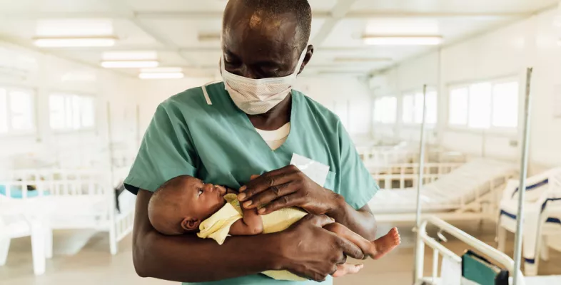 Ein Krankenpfleger in Sierra Leona hält ein Neugeborenes.