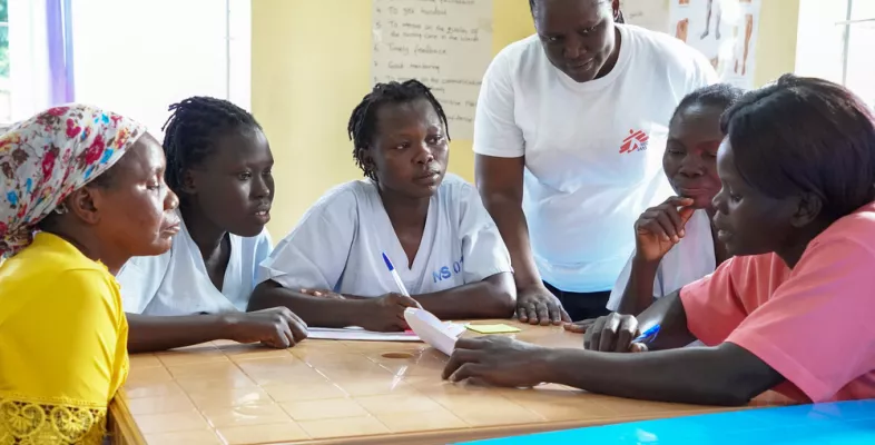 Mitarbeitende sitzen an Tisch, eine Person spricht.