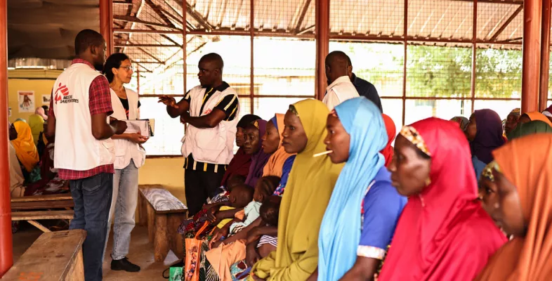 Patient*innen warten auf Bänken, daneben sprechen Mitarbeitende