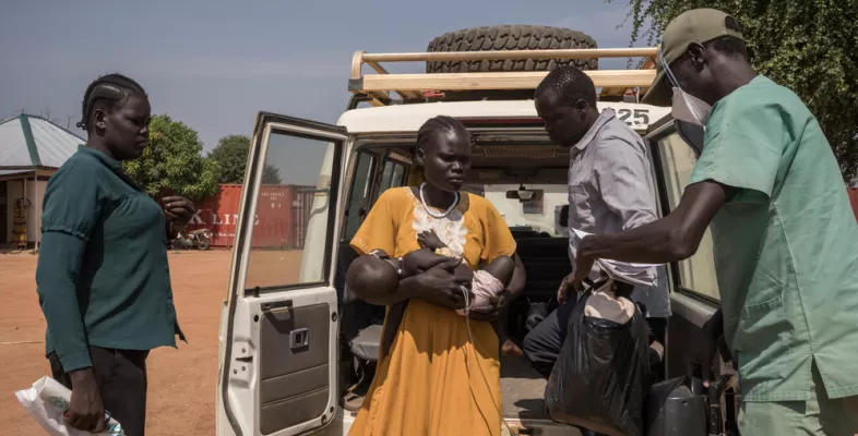 Frau mit Baby steigt aus Krankenwagen, daneben zwei Mitarbeitende