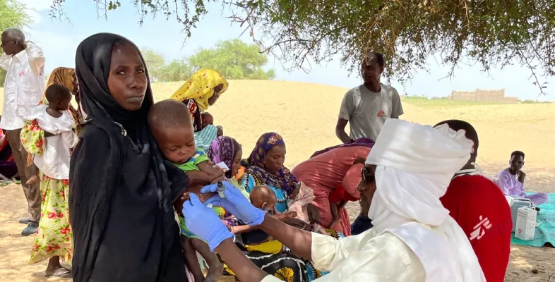 Mutter hält Kind während Untersuchung auf dem Arm unter einem Baum
