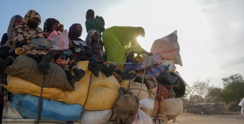 Mehrere Menschen sitzen dicht gedrängt auf einem überladenen Transporter.