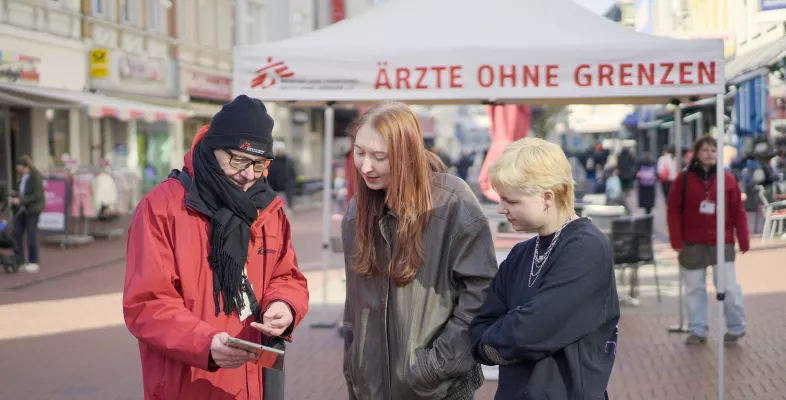 Drei Personen reden vor einem Ärzte ohne Grenzen Info-Stand