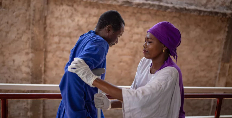 Man läuft mit Krücke während Physiotherapeutin ihn stützt