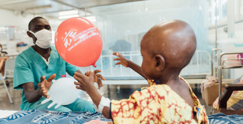 Verschenken Sie eine Spende und unterstützen Sie damit Projekte wie unser Kinderkrankenhaus in Kenema, Sierra Leone. Pfleger bringt kleinen Patientin einen Luftballon