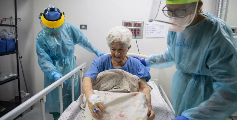 Alte Frau wird von zwei Pflegern in Schutzkleidung betreut