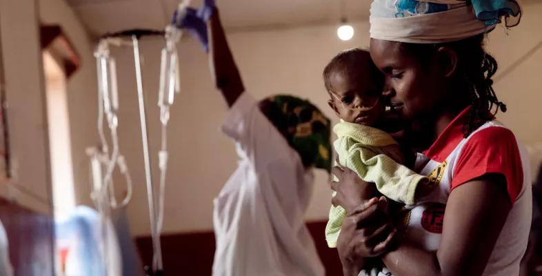 Zentralafrikanische Republik: Mutter hält ihr krankes Kind im Arm. Im Hintergrund ein Mitarbeiterin und Infusionen