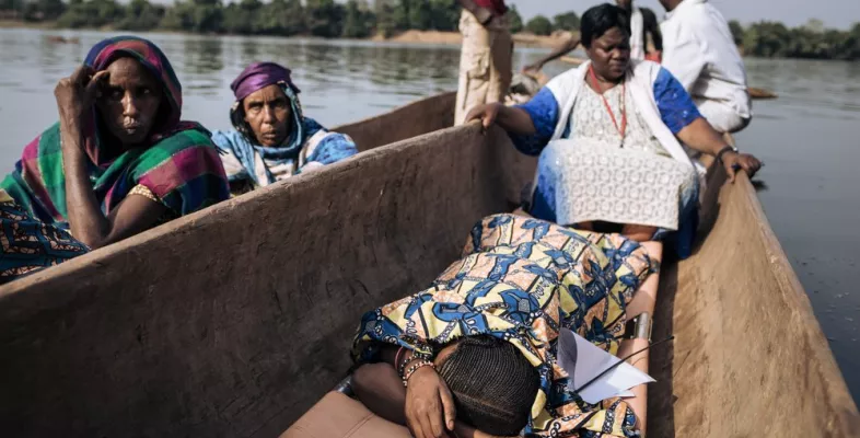 Mehrere Menschen in einem Kanu, eine Frau liegt auf einer Liege auf dem Boden