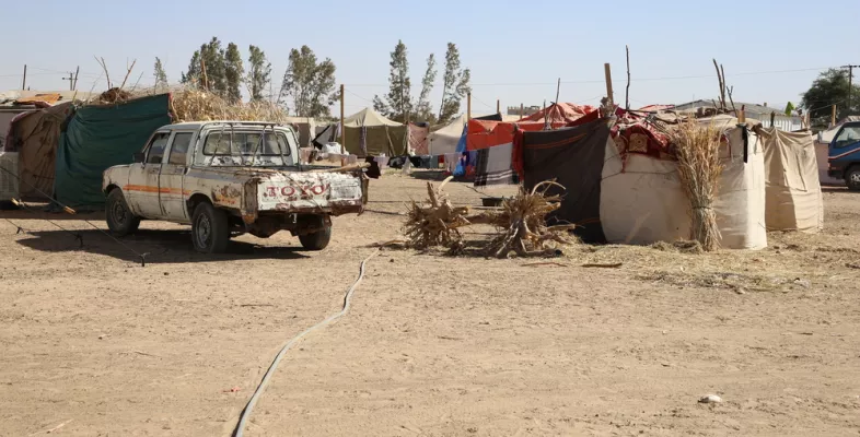 Ein altes Auto vor einem Camp mit vielen Zelten in einer wüstenähnlichen Landschaft