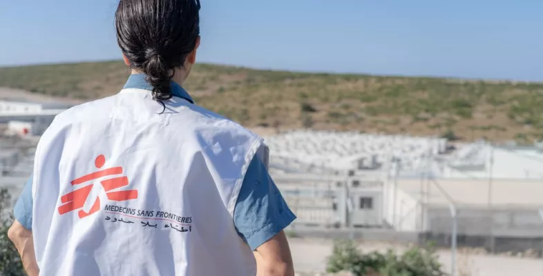 Eine Person von hinten fotografiert, mit einer Ärzte ohne Grenzen Weste die auf ein entferntes Camp schaut