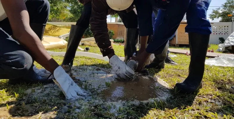 Drei Mitarbeitende von Ärzte ohne Grenzen mit Helmen buddeln ein Loch