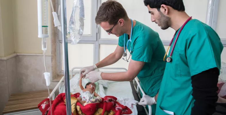 Zwei Mitarbeiter kümmern sich um ein Neugeborenes in einem Bett