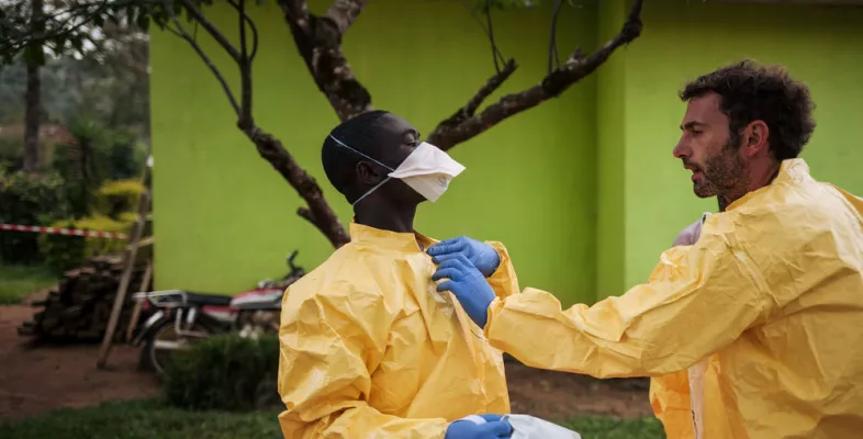 Unser Hygienespezialist Luca Fontana erklärt einem Kollegen in Kalunguta, D.R. Kongo, wie sich die Ebola-Gesundheitsteams gegen das Virus schützen können. Hygienespezialist hilft Kollege in Schutzkleidung