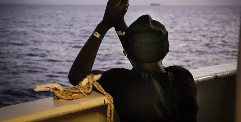 An der Reling der Sea Watch 4 schaut eine gerettete Person aufs Meer