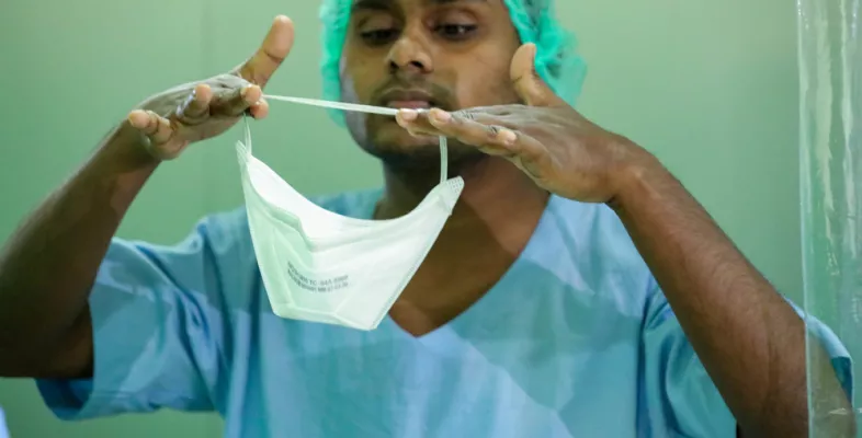 Mann in OP-Kleidung zieht FFP2-Maske an