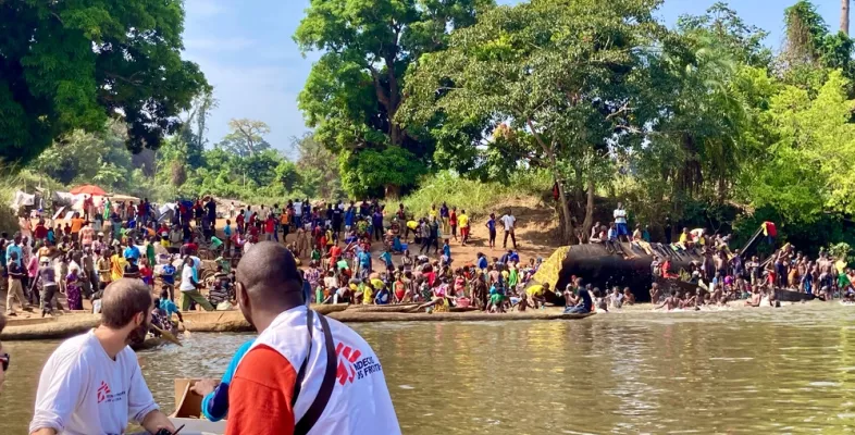Zwei Männer auf Boot fahren ans Ufer zu Menschengruppe