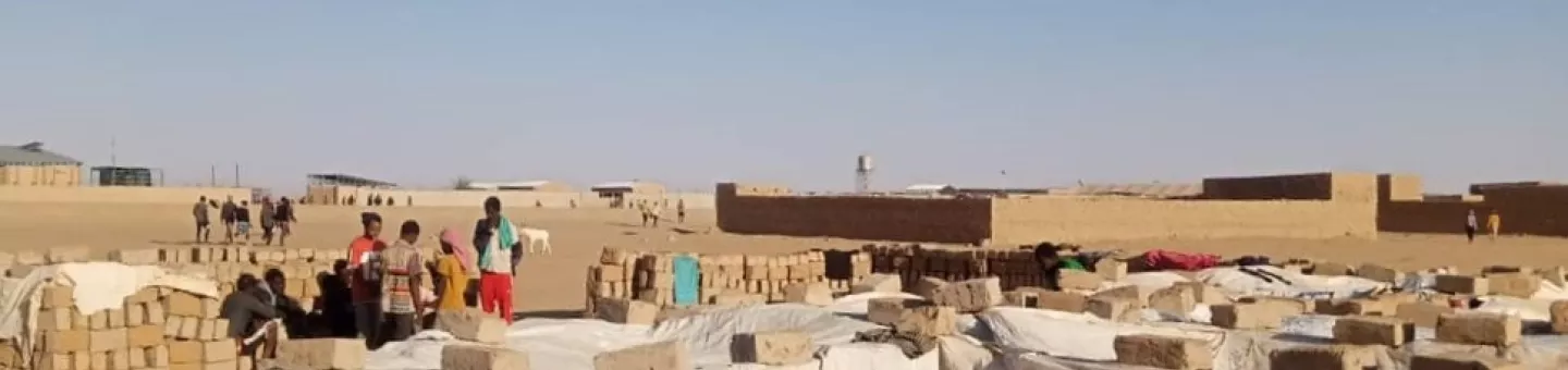 Menschen stehen in der Wüste Nigers auf einer offenen Fläche mit provisorischer Behausung.