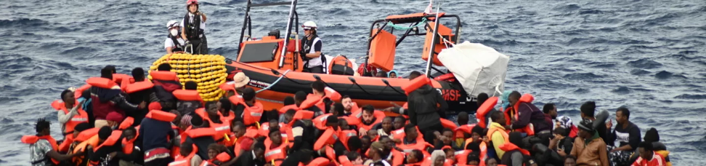 Ein Schlauchboot liegt neben einem massiv überfüllten Holzboot