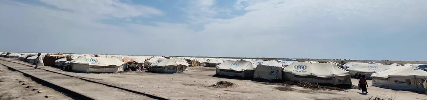 Weite Aufnahme von einem Camp für geflüchtete Menschen. Viele weiße Zelte und eine entfernte, laufende Person.