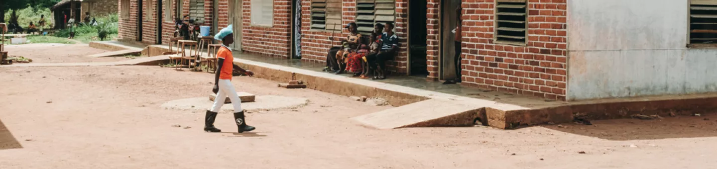 Ein flacher Gebäudetrackt, davor Sandweg und ein laufende Person.