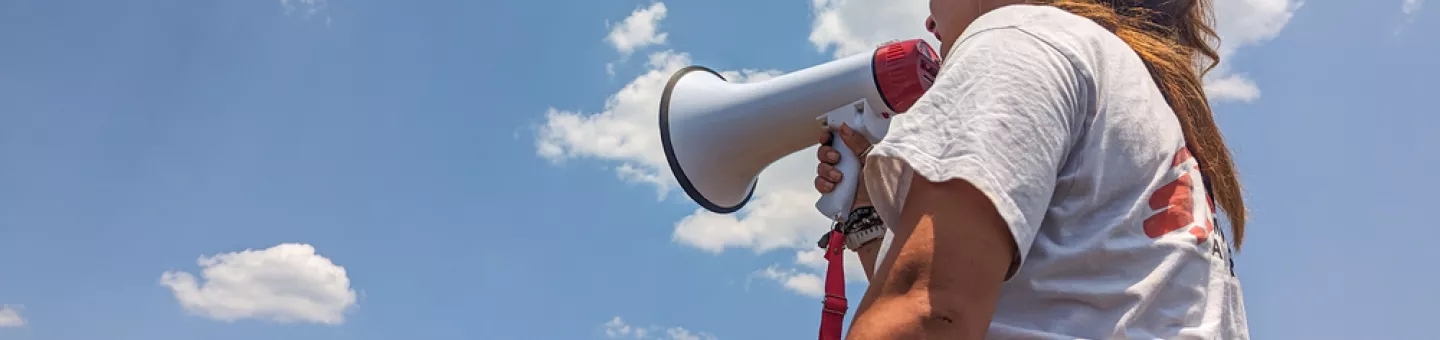 Wir leisten medizinische Notversorgung für Ankommende auf Lesbos. Eine Person von hinten in Ärzte ohne Grenzen Shirt mit Megaphone