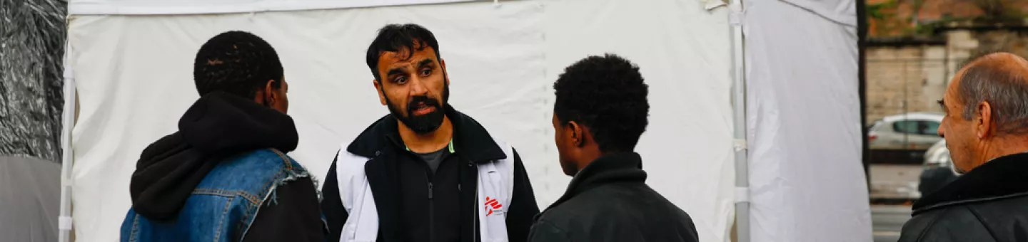 Migranten und ein Mitarbeiter vor einer mobilen Klinik in Calais