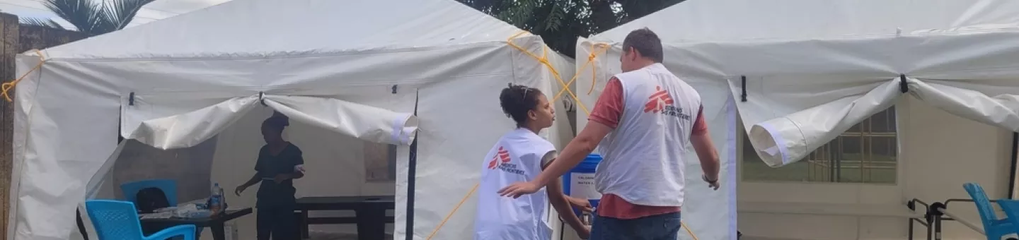 Zwei Mitarbeitende vor einem Zelt, in dem Cholera behandelt wird.