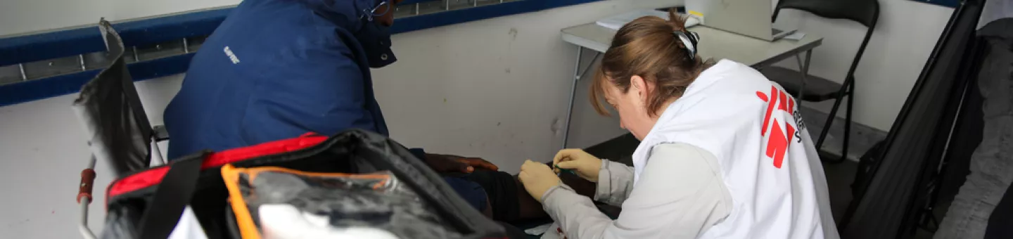 Mitarbeitende beugt sich über Beine von sitzender Person 