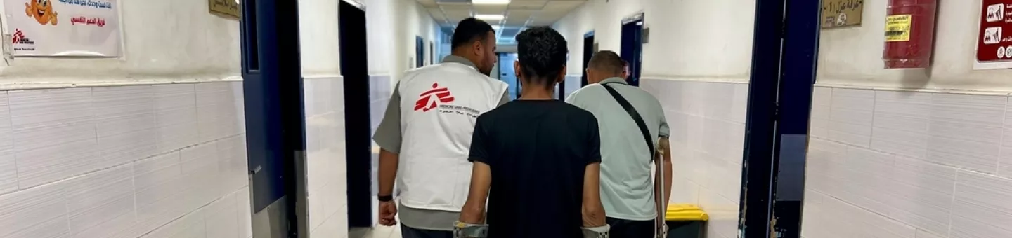 Mitarbeitende und Patient auf Krücken in Krankenhausgang