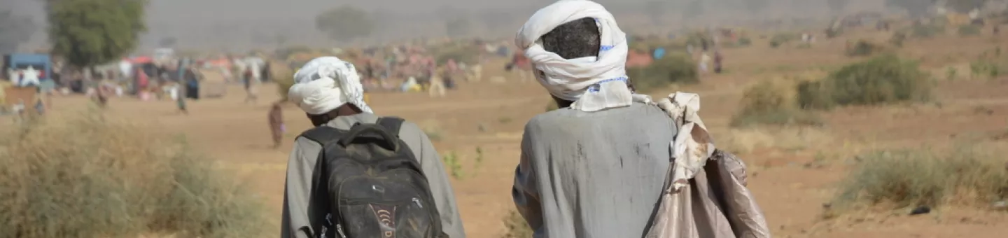 Zwei Männer gehen schwer bepackt durch eine trockene Landschaft