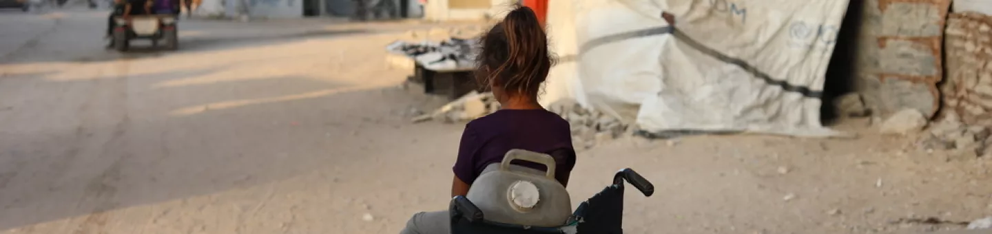 Kleines Mädchen sitzt in Rollstuhl mit Wasserkanister