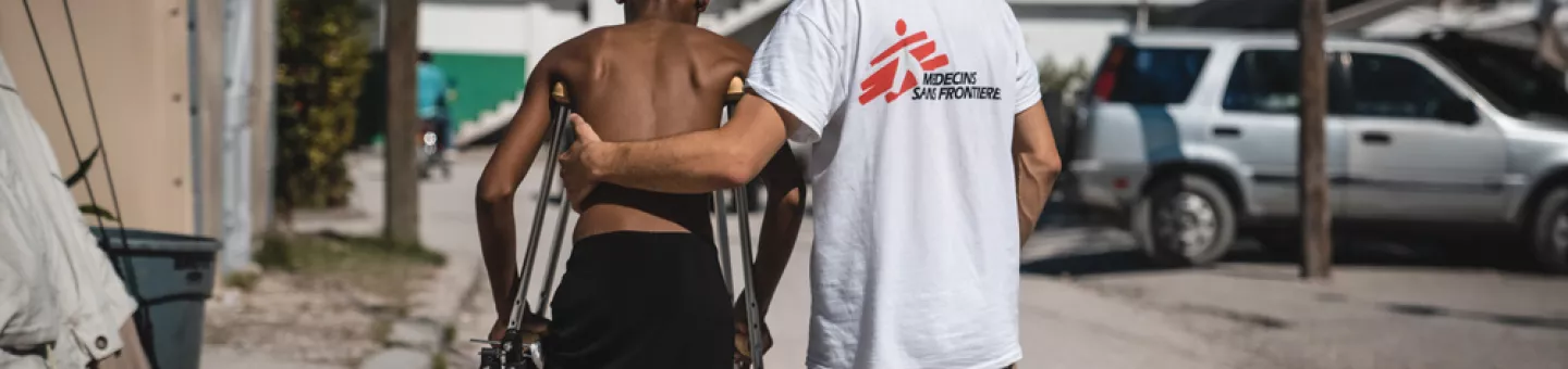 Ein Mitarbeiter von Ärzte ohne Grenzen stützt einen Mann auf Krücken