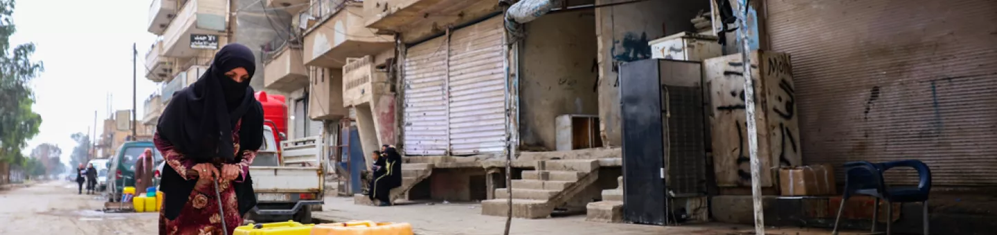 Eine Frau transportiert zwei Wasserkanister auf einem Karren durch eine Straße.