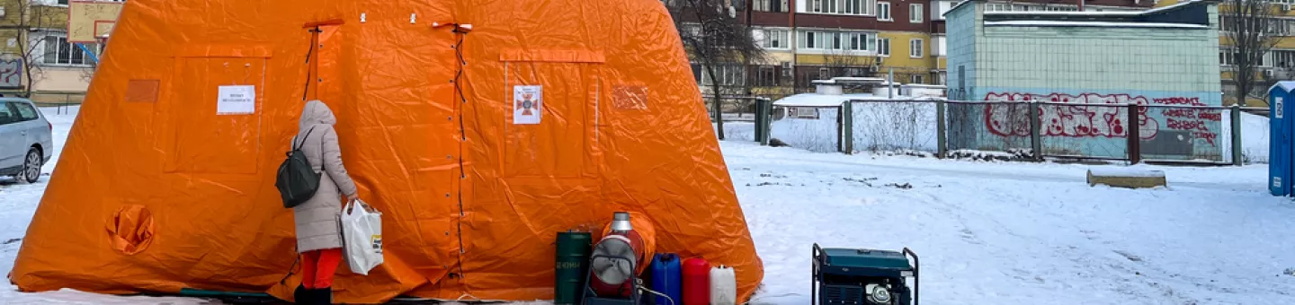 Zelt im Schnee - davor Person neben Generator