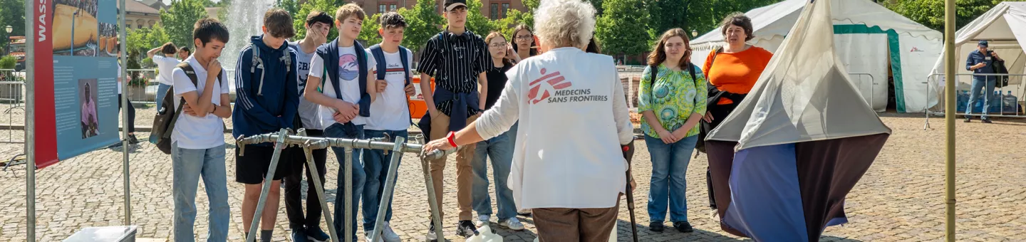 Mitarbeitende spricht vor Ausstellungsbesuchenden auf offenem Platz