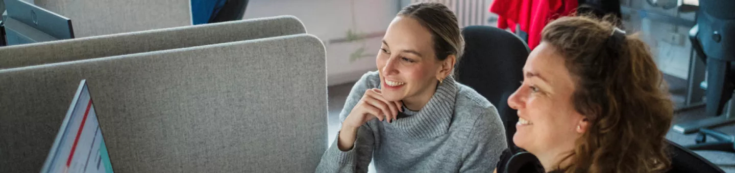 Zwei Mitarbeitende am Schreibtisch vor dem Computer