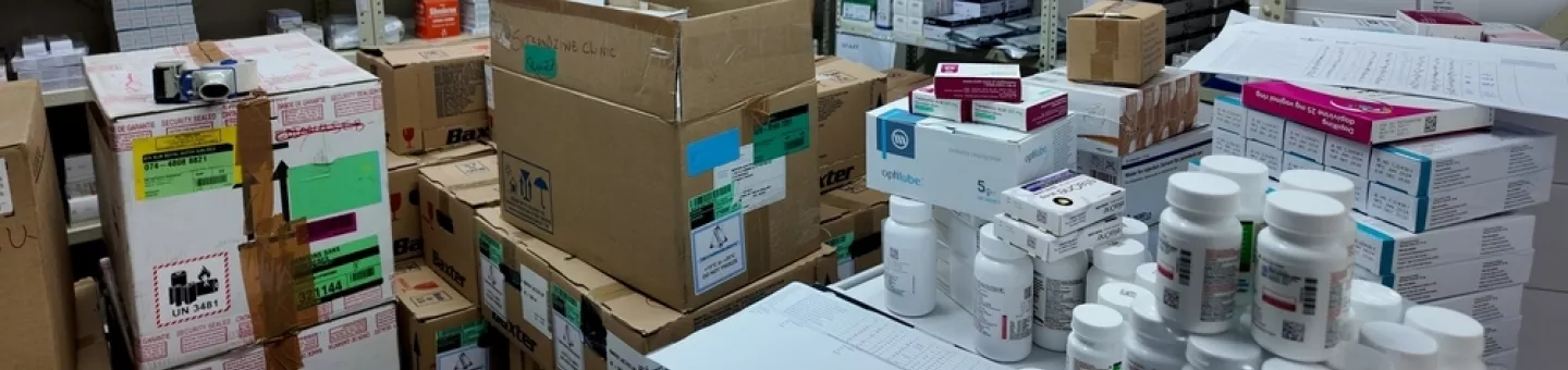 Lagerraum einer Klinik-Apotheke mit Regalen voller Medikamentenschachteln und Kartons sowie Arbeitsfläche mit Arzneiflaschen.