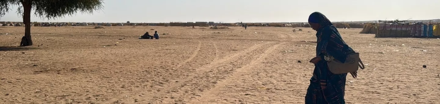 Eine Frau geht alleine über eine freie sandige Fläche.