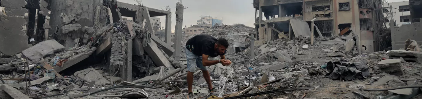 Ein Mensch an Wasserleitung zwischen den Trümmern zerstörter Gebäude