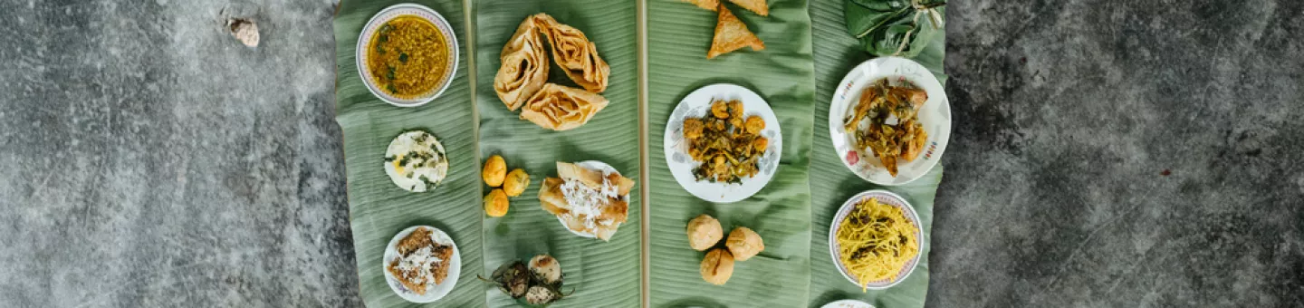 verschiedene Speisen auf großem Pflanzenblatt vor grauem Hintergrund