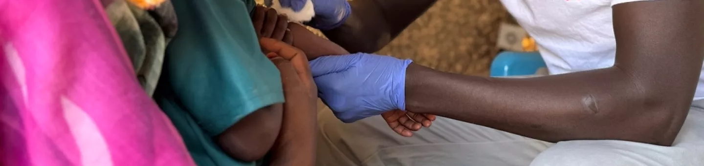 Mitarbeiter impft ein Kind welches im Arm der Mutter liegt