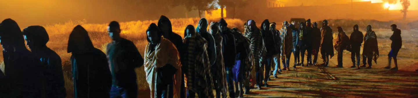 Zahlreiche Menschen stehen in der Dämmerung in einer langen Schlange