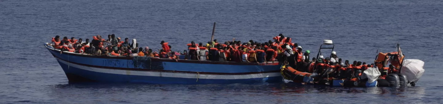 232 in Seenot geratene Menschen mit Rettungswesten auf einem Holzboot im Mittelmeer