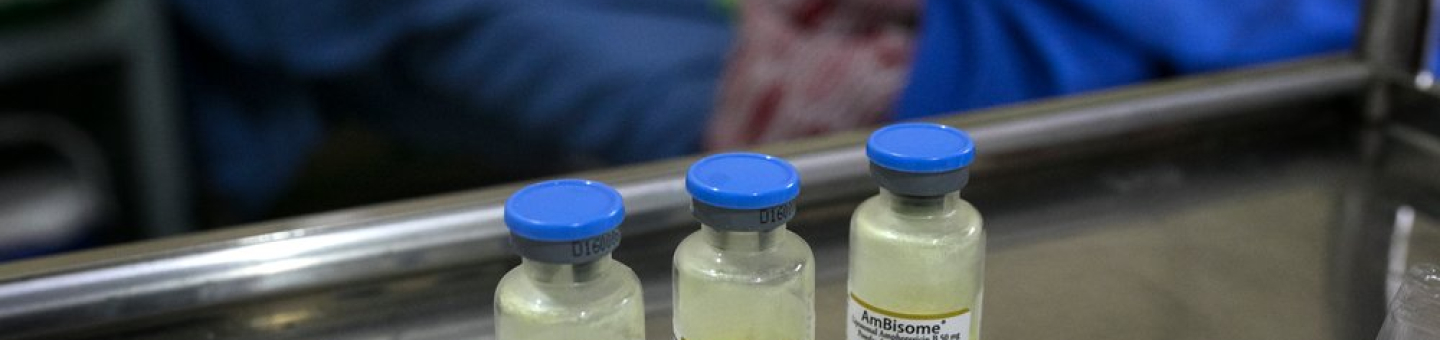 Amphotericin B, das zur Behandlung von Kryptokokken-Meningitis eingesetzt wird. Drei Impfampullen stehen auf einem Tisch in einem Krankenhaus. Im Hintergrund ist eine Patientin zu sehen.