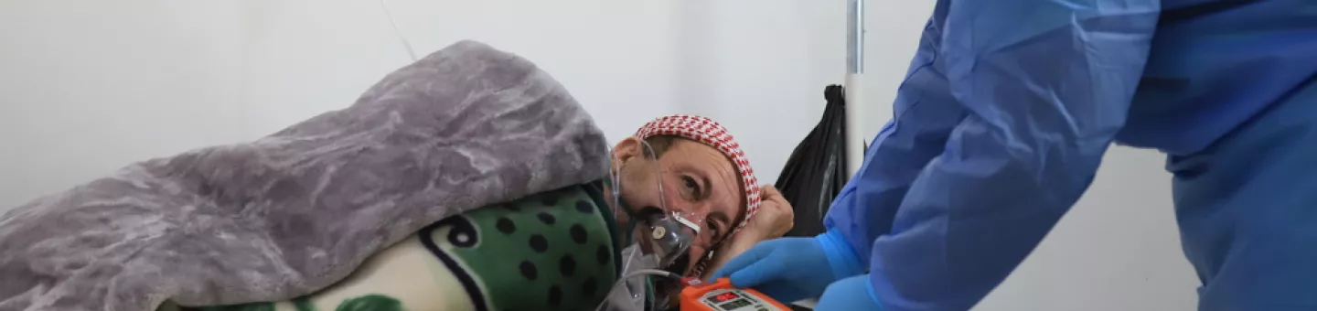 Ein Mann in blauem Schutzanzug beugt sich zu einem Mann herunter, der künstlich beatmet wird